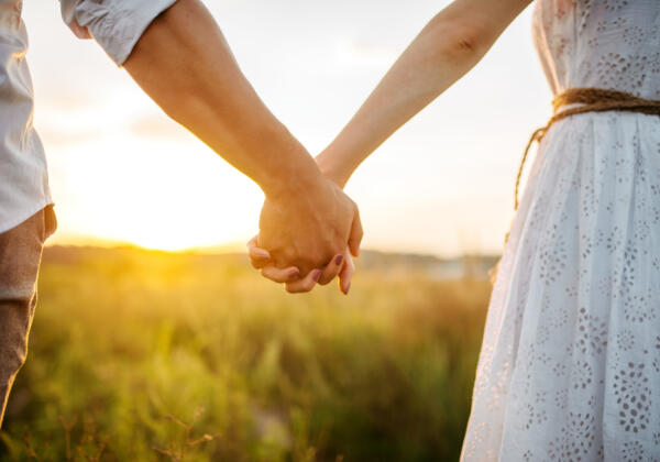 Couple,hold,hands,in,green,field,on,sunset